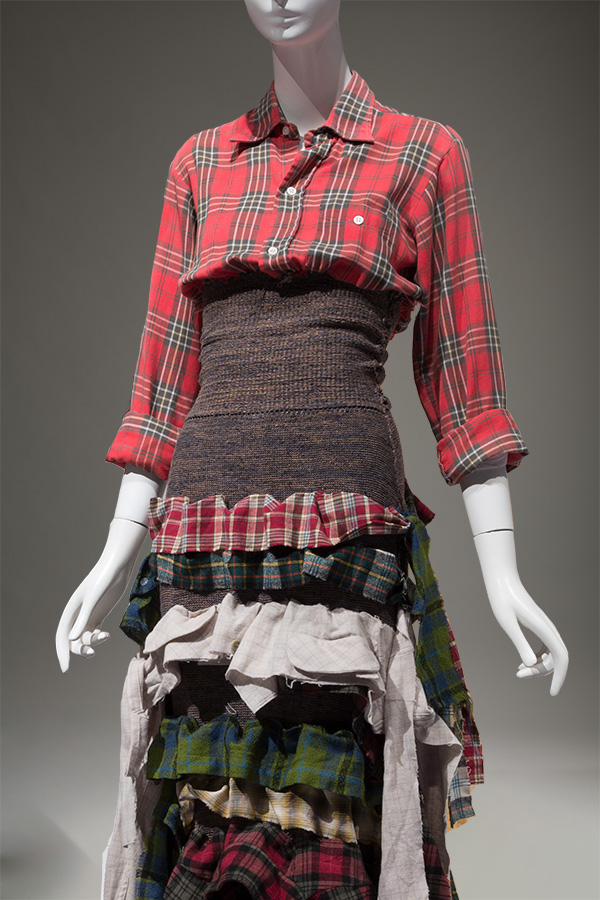 long sleeved red plaid button down dress with brown knitted bodice and skirt composed of layered, multicolored plaid tops