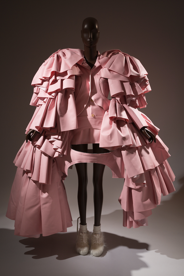 extravagant and unusual ensemble in multiple folds of pink pleather that includes a short jacket dress with broad shoulders and faux pleated paniers that extend below the knee