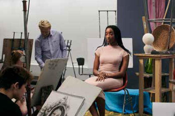 a model posing for art studio class, she is seated on a stool in the middle of the room, and is surrounded by drawing students at their easels and benches. There are patches of color throughout the composition, such as a turquoise drapery set for a still life, that's adjacent to the model's pale pink dress.