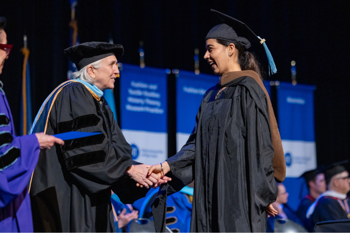 Vice President for Academic Affairs shakes hand of graduate student in regalia onstage at Master's Commencement