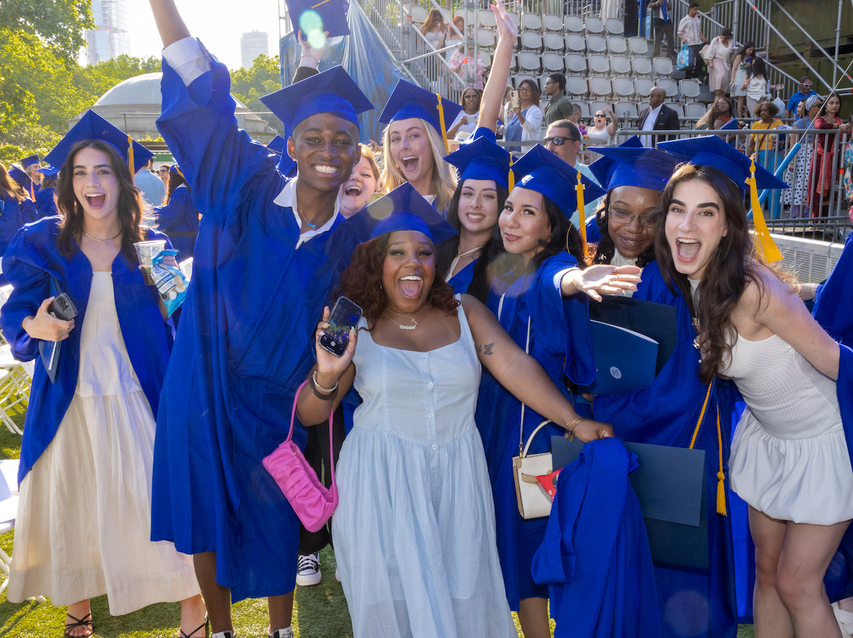 students in blue cap and gown cheer at FIT's 2024 commencement