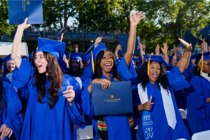 three students in regalia cheering with hands up, also holding diploma folders