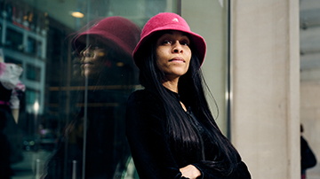 Student with pink Kangol hat standing outdoors on campus