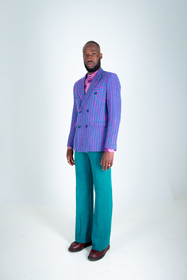 Black man waring blue and purple pinstripe suit jacket with teal trousers