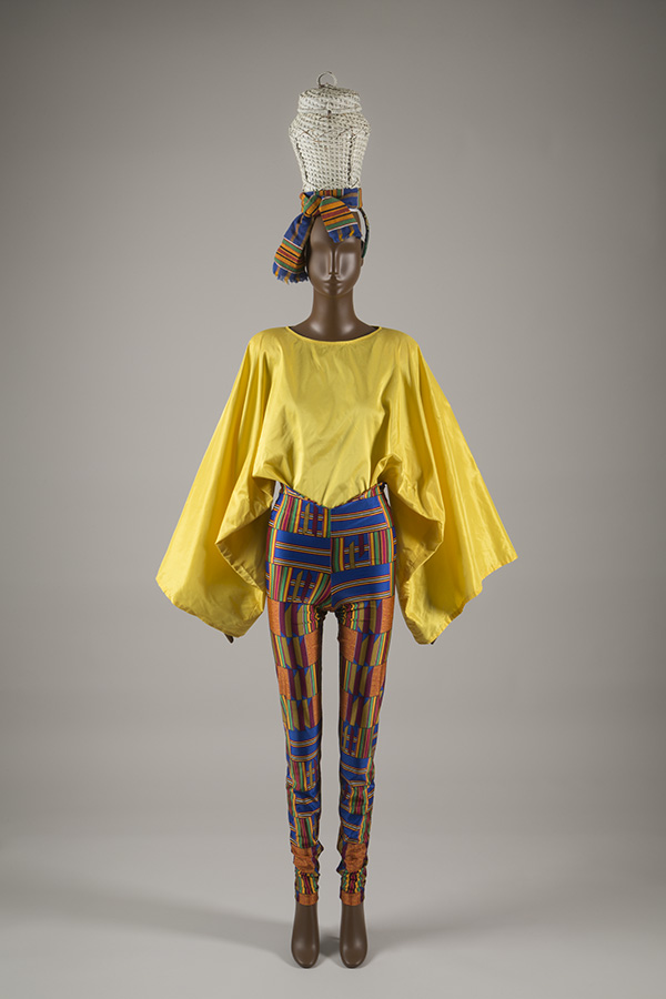 ensemble of a basket hat, yellow top with large sleeves, and multi-colored kente print trousers