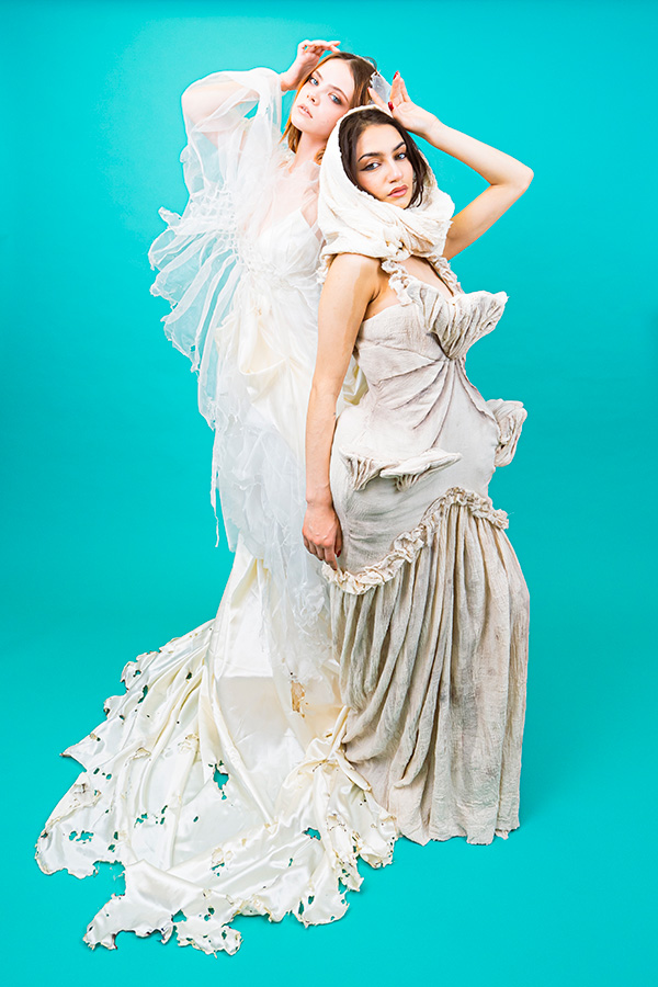 two women posing back to back, wearing white dresses