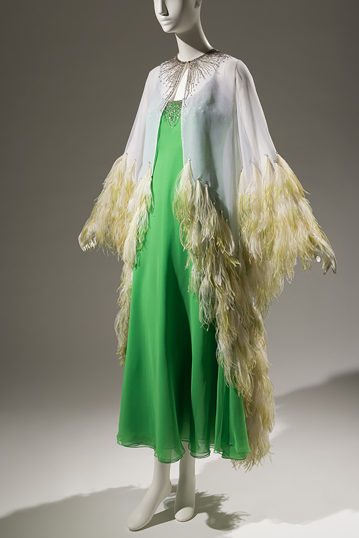 green dress with white, sheer cape with gold rhinestones and yellow ostrich feathers at end of sleeves and trim