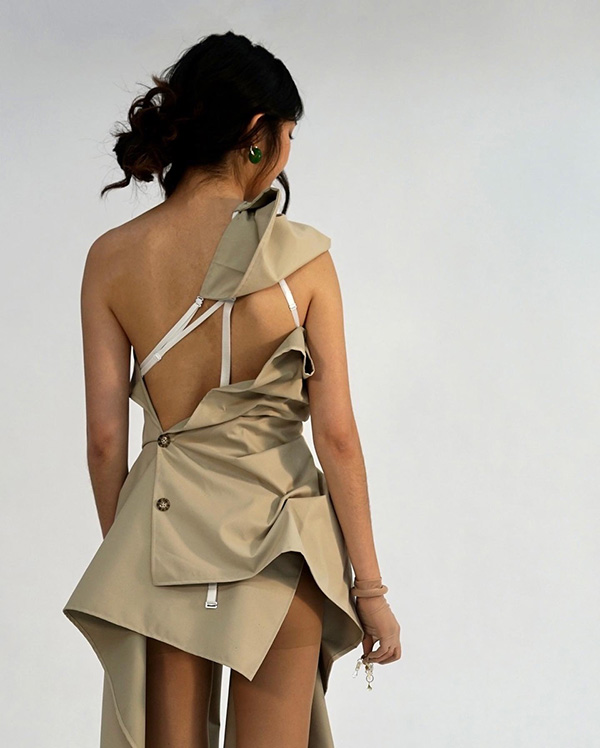 Back view of model wearing a beige dress, made to look like a deconstructed, ruched trench coat.