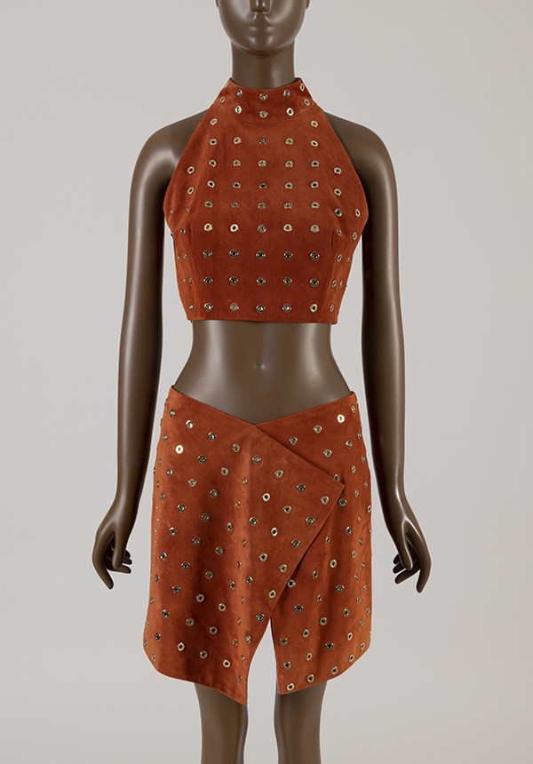 Mannequin in a orange / brown suede midriff halter top decorated with gold grommets and paired with a wraparound skirt