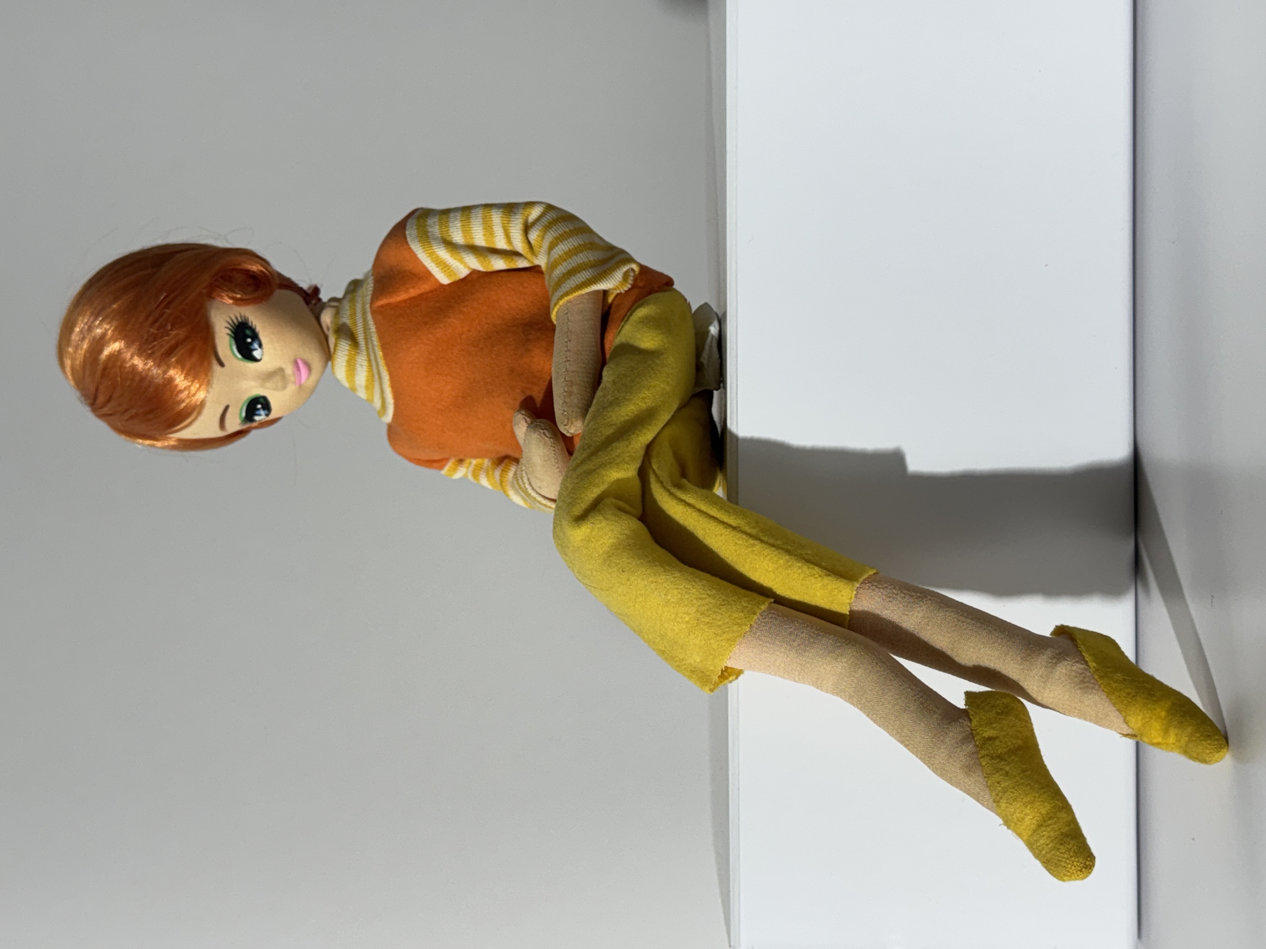 60's doll with short, orange hair wearing an orange turtleneck with yellow and white stripes on neck and sleeves with yellow pants and yellow flats, posed in a seated position